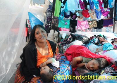 Julia, vendor of lingerie, breast-feeds her baby boy while her other son sleeps.